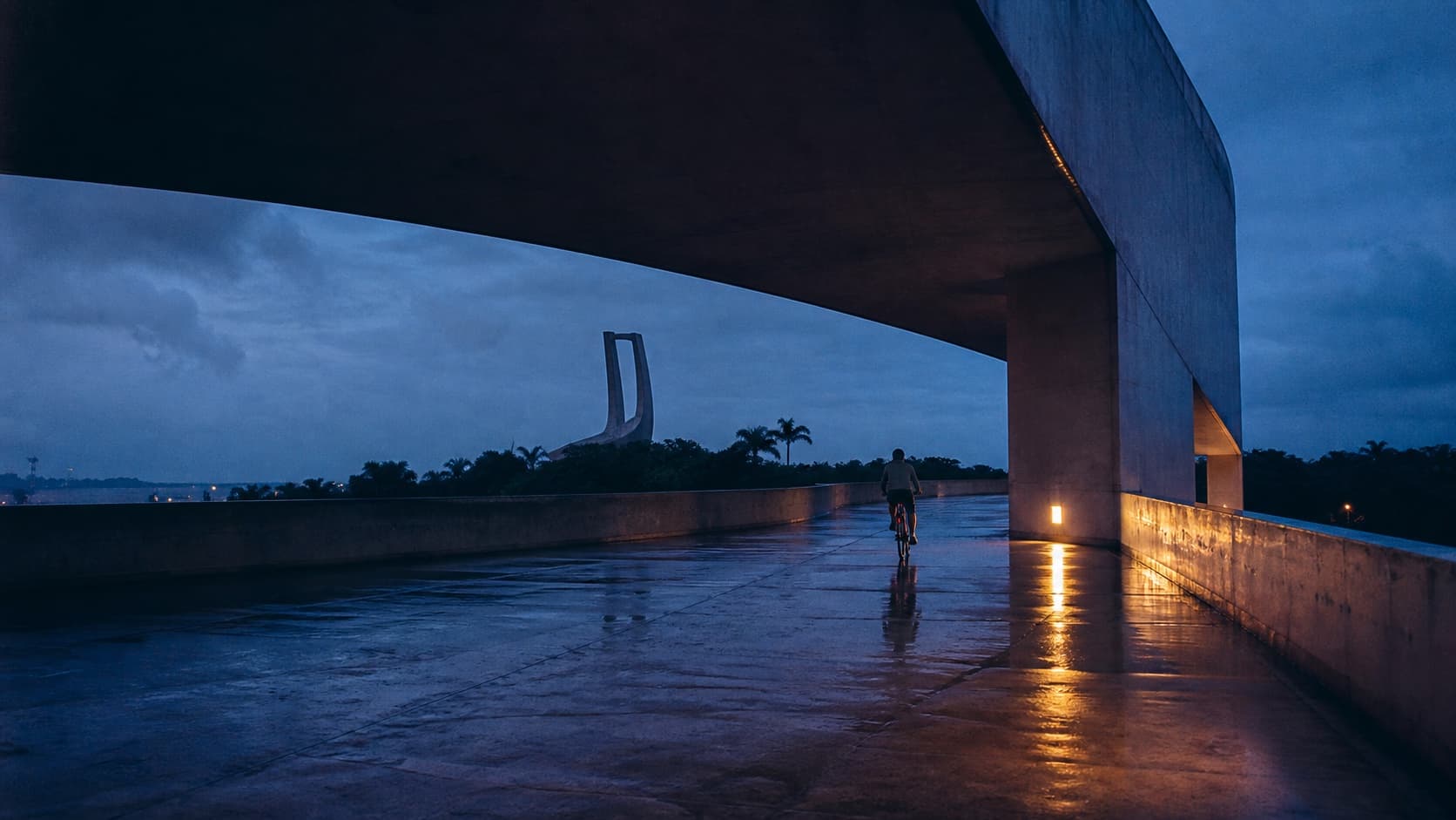 Ciclista atravessando arquitetura de concreto ao anoitecer